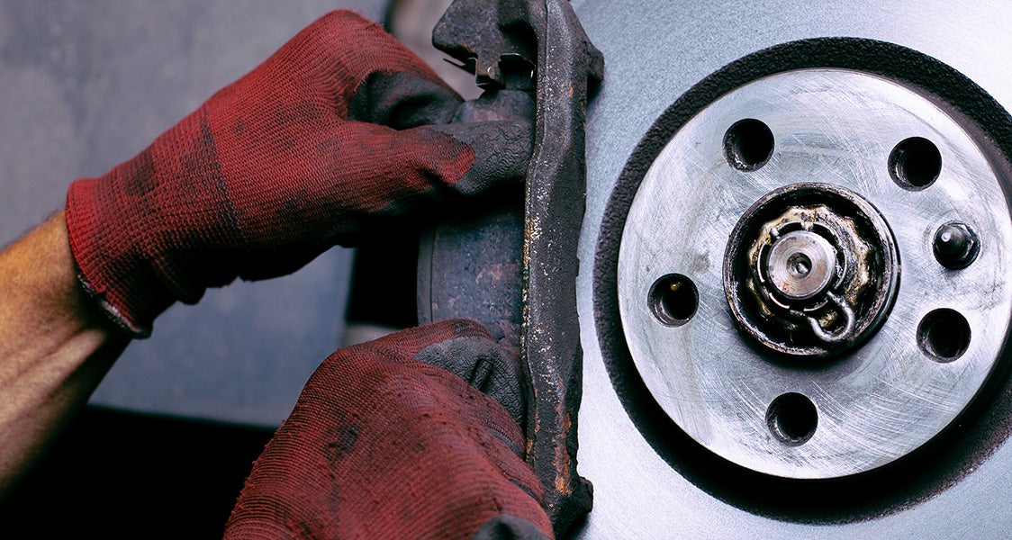 A person in red work gloves replacing worn brake pads on a car's disc brake assembly.