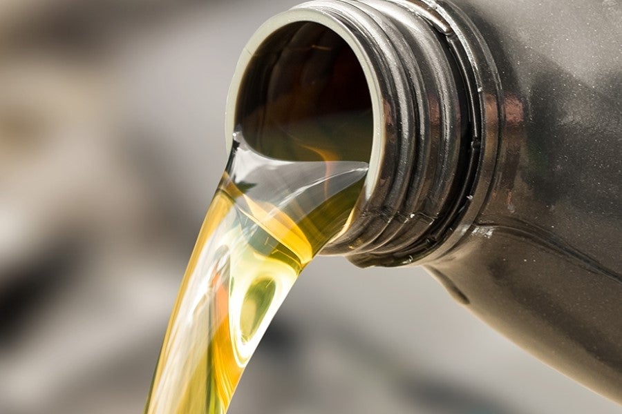 Golden-yellow oil pours in a thick, continuous stream from the threaded neck of a dark bottle.